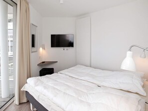A modern hotel room with a large bed, a television mounted on the wall, a bedside table, and a window with curtains.