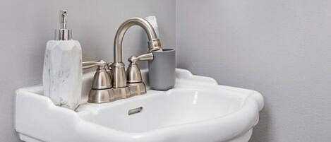 A white bathroom sink with a single faucet and a marble soap holder.