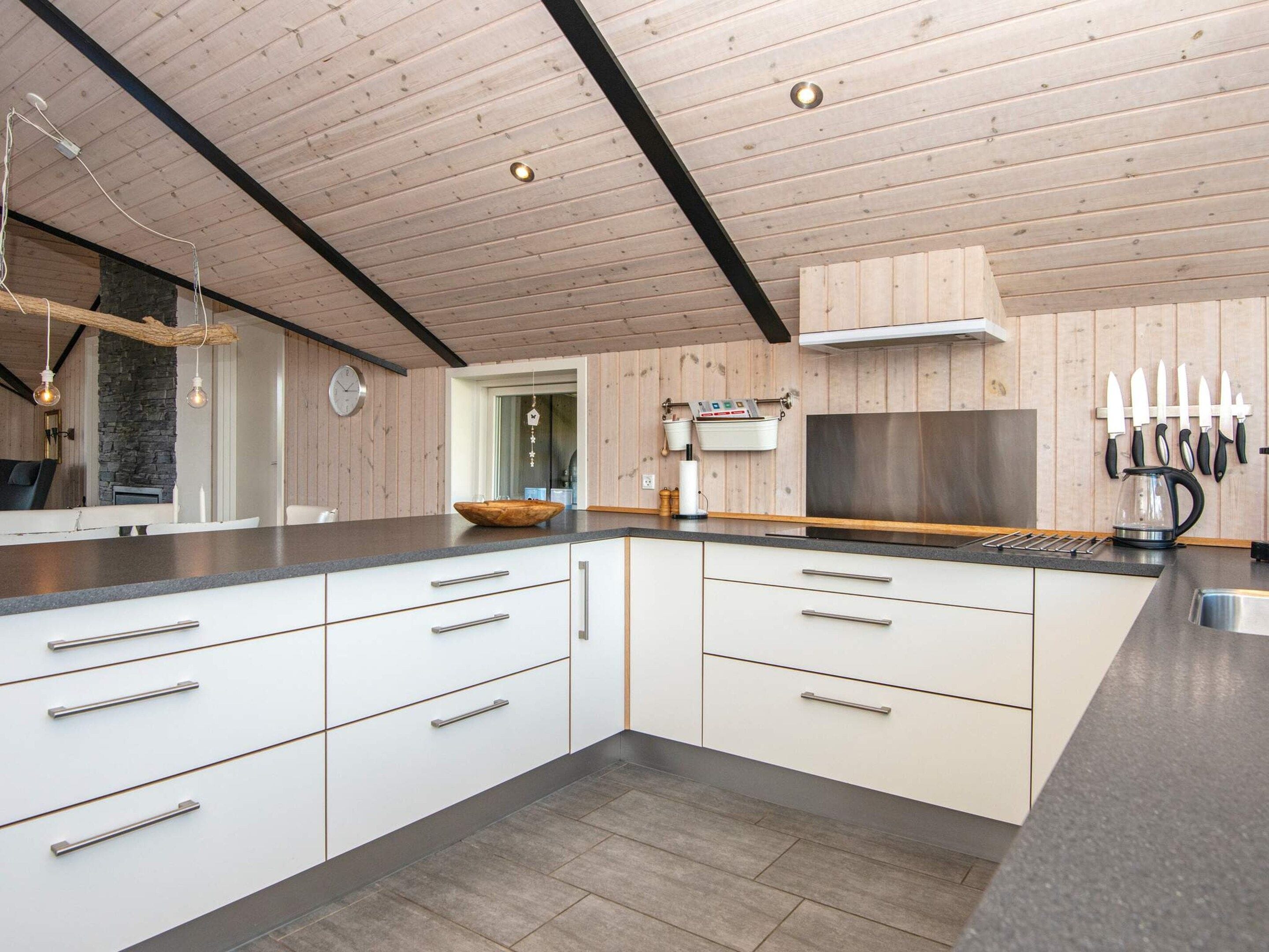 A modern kitchen with a large island, wooden ceiling, and a stone accent wall.