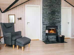A cozy room with a stone fireplace, a grey upholstered armchair, and a matching ottoman. - 7 Person Holiday Home in Hejls (Hejls)