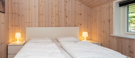 Una cama doble con dos mesitas de noche, cada una con una lámpara, en una habitación con paneles de madera y techo inclinado.