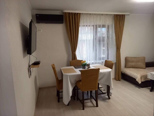 A dining area with a table set for four, surrounded by wicker chairs. A television is mounted on the wall to the left. - Guest House & Rooms Chris Toros (Teteven)
