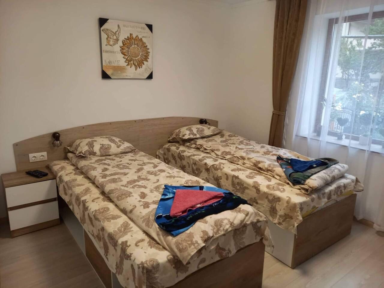 A double bed with floral bedding, a bedside table with a lamp, and a window with curtains.
