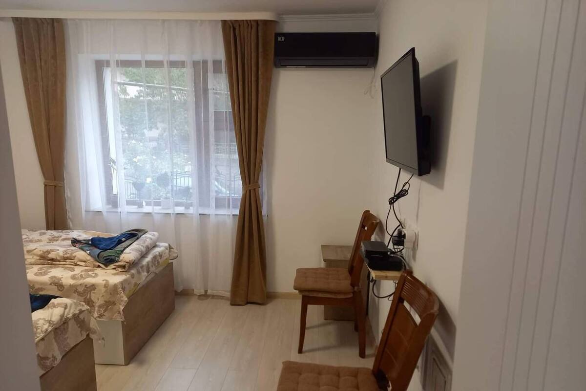 A bedroom with a bed, a desk with a chair, a TV, and an air conditioning unit.