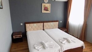 A double bed with a wooden frame and beige headboard, two bedside tables, a wall-mounted air conditioner, a framed picture, and a window with curtains.