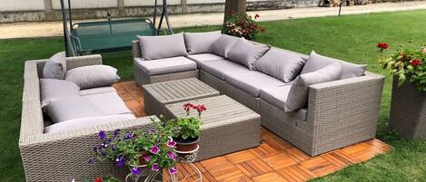 A sectional sofa set with cushions, a coffee table, and a wicker planter with flowers on a wooden deck.