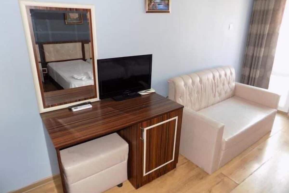 A hotel room with a wooden desk, a television, a sofa, and a mirror.