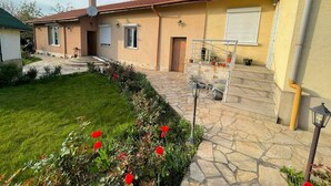 A house with a stone pathway leading to the entrance, a small garden with red flowers, and a metal gate.