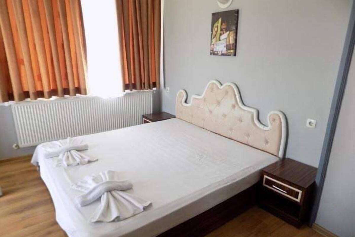 A neatly made bed with a headboard, a small bedside table, and a picture on the wall.