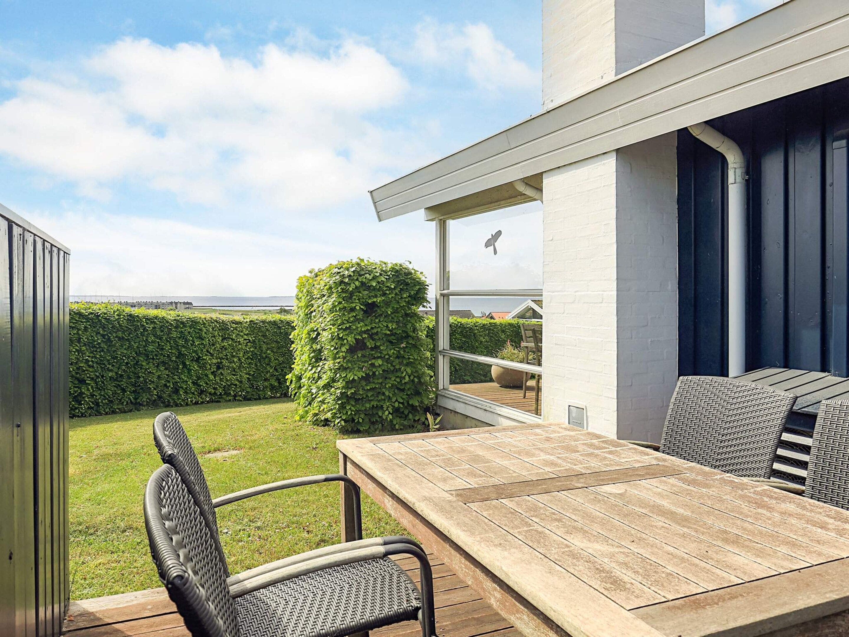 Une terrasse avec une table et des chaises, une vue sur la mer et une haie.