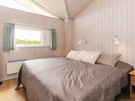 Un dormitorio con cama, ventana con cortinas, radiador y lámparas fijadas a la pared.