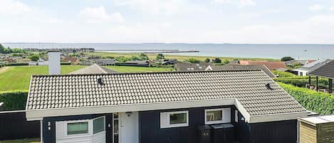 A modern two-story house with a tiled roof, a front porch, and a view of the sea.