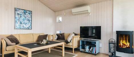 A cozy living room with a sofa, a coffee table, a flat-screen TV, a bookshelf, and a fireplace.