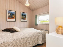 A bedroom with a bed, two framed artworks, a window with a view, a lamp, and a radiator.