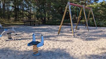 A sandy playground with a swing set and a seesaw.