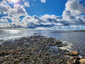 A rocky shoreline with a clear sky and sunlight reflecting off the water.