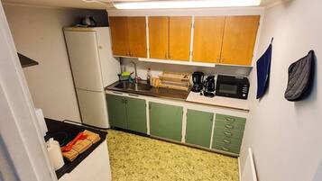 Cocina compacta con refrigerador, microondas, cafetera y armarios de madera.