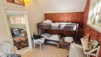 A compact room with bunk beds, a small table, a chair, and a radiator.
