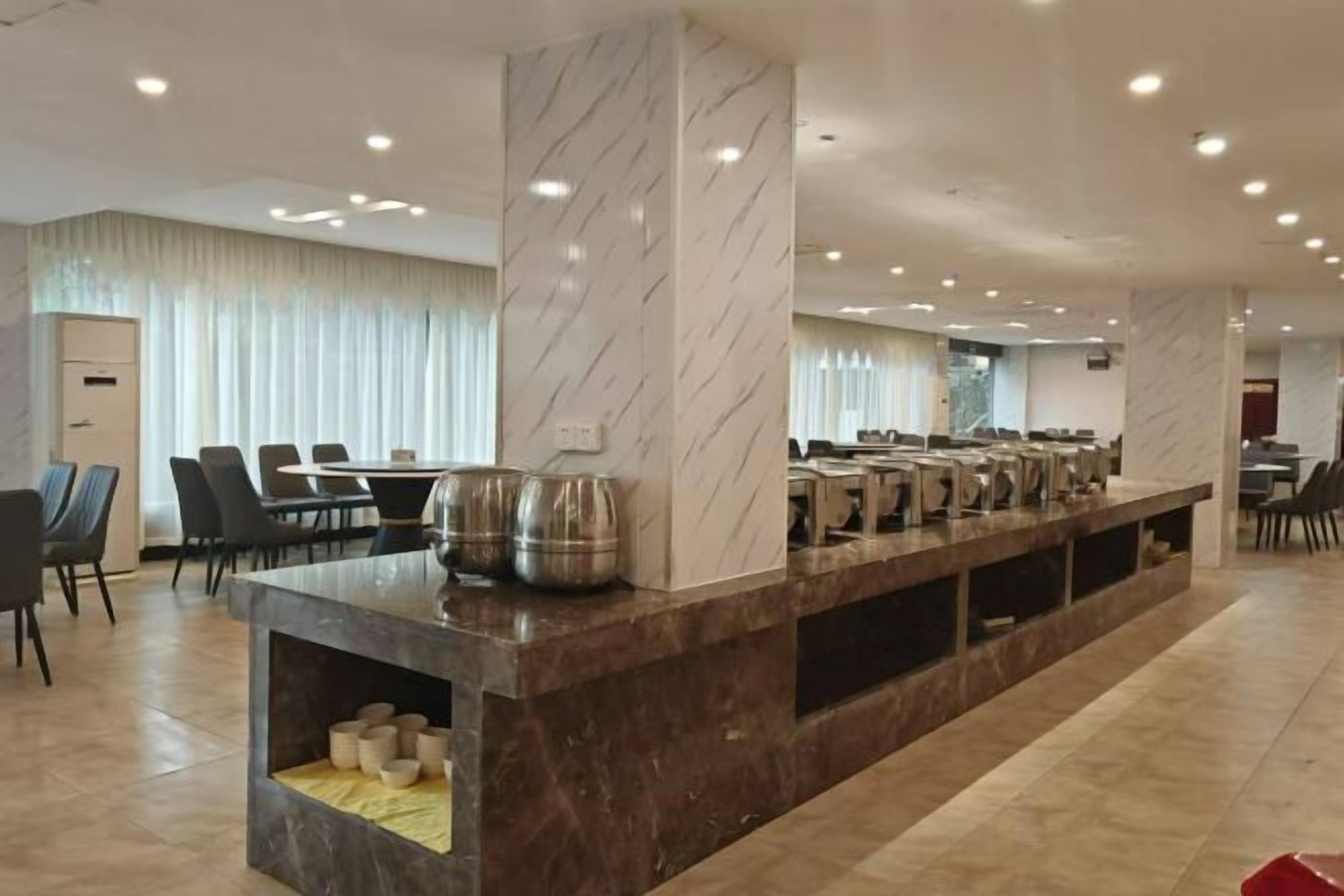 Un hall d’hôtel moderne, doté de colonnes en marbre, d’un long comptoir de réception et de plusieurs tables à manger.