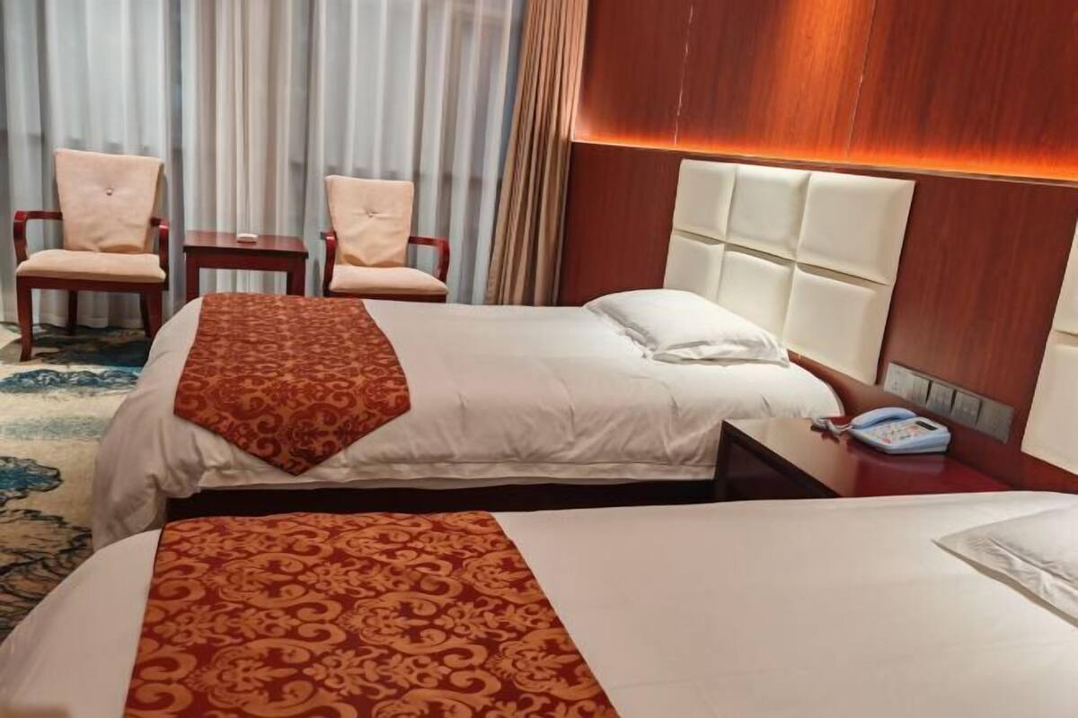 A hotel room with two beds, a wooden headboard, a bedside phone, and a pair of chairs.