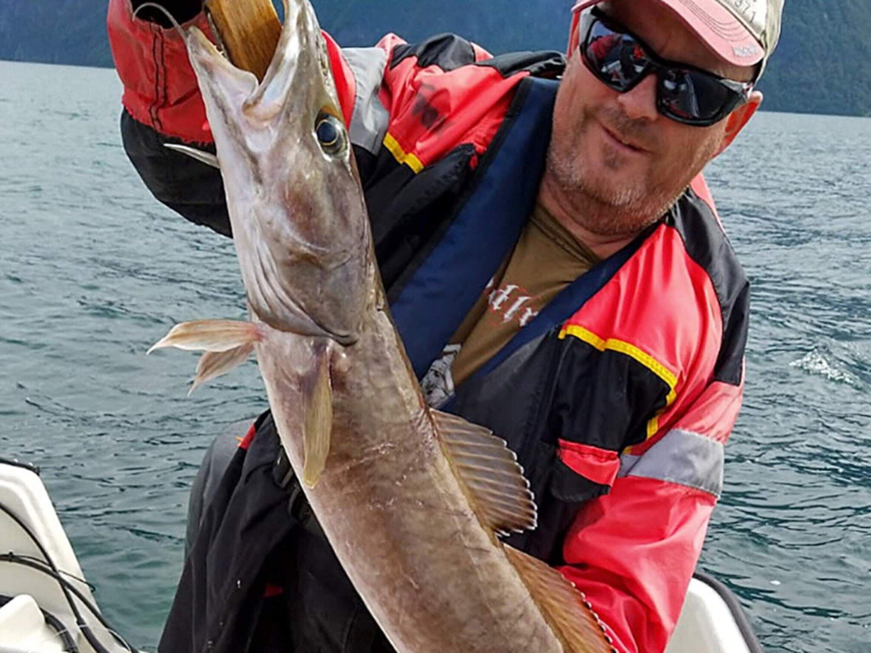 A person holding a large fish, wearing a life jacket and a cap, on a boat.