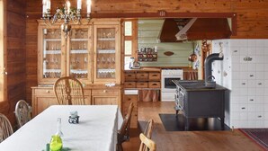 A wooden cabin interior with a dining table, chairs, a kitchen area with a stove, and cabinets. - 8 Person Holiday Home in Orskog (Ålesund)