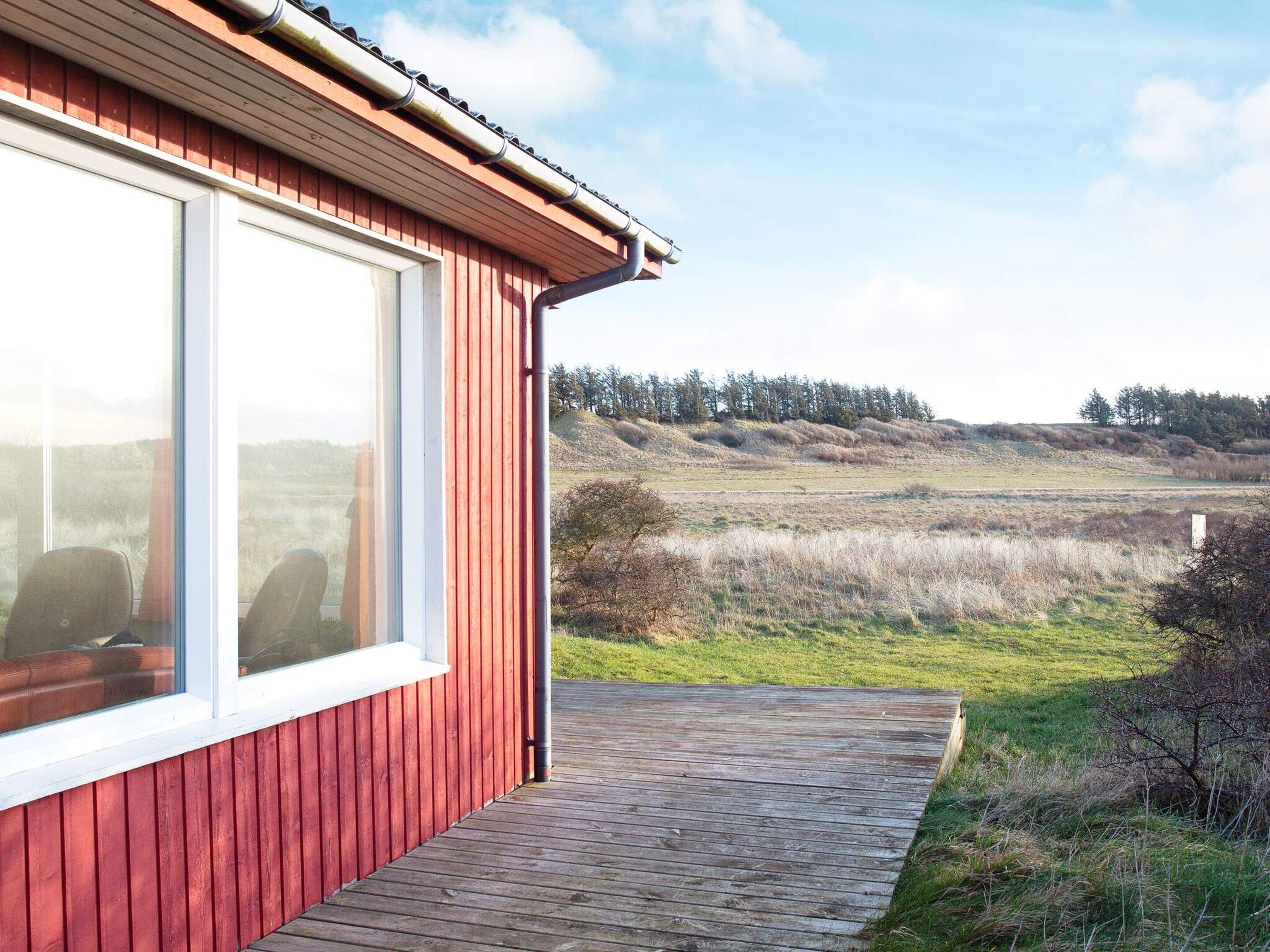 En rød bygning med et stort vindue og en træterrasse.
