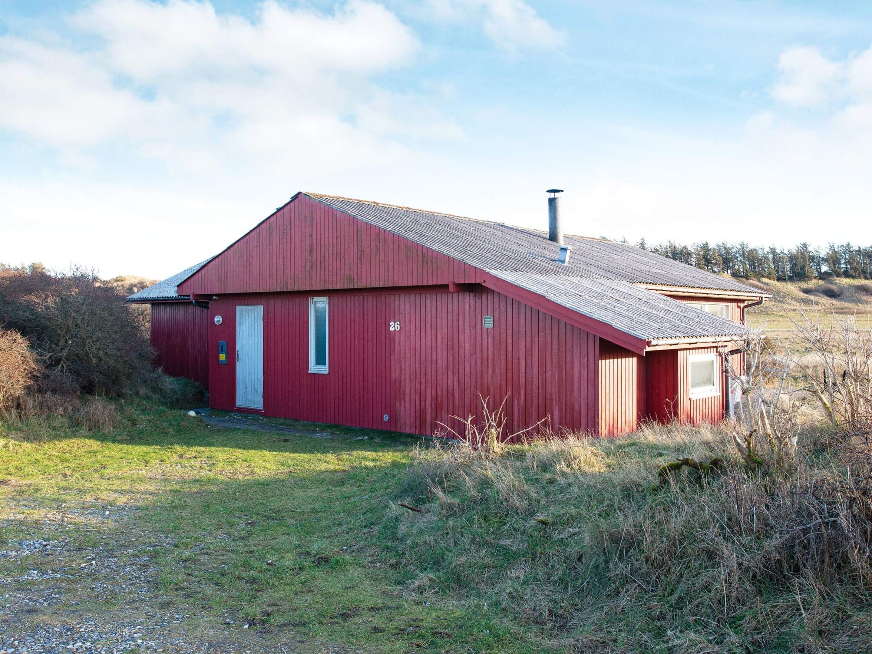 En rød lade med skråt tag og skorsten, omgivet af græsareal og sparsom beplantning.
