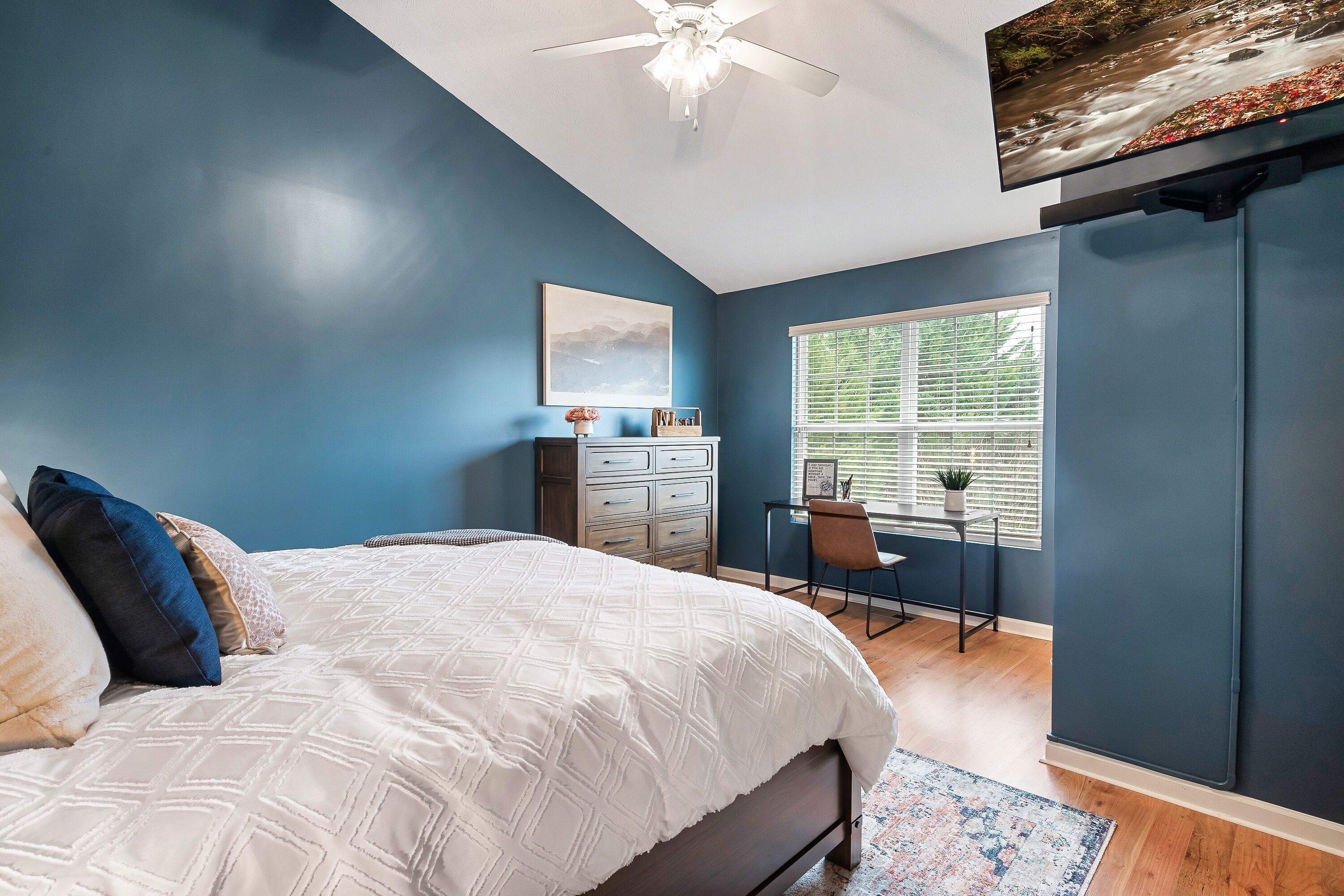 A bedroom with a bed, a desk, and a window.