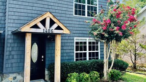 A two-story house with a dark siding exterior, a front porch with a wooden railing, and a number "1406" displayed above the door.