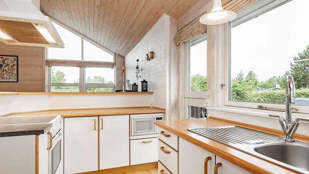 Eine moderne Küche mit Holzschränken, einer Edelstahlspüle und einem Fenster mit Blick auf Grünflächen.