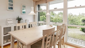 A dining area with a wooden table and chairs, large windows with curtains, and a view of greenery outside. - 6 Person Holiday Home in Hals (Hals)
