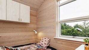 A bedroom with wooden walls, a bed with a colorful blanket, a nightstand with a lamp, and a window with a view of greenery. - 6 Person Holiday Home in Hals (Hals)