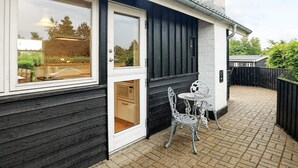 A modern building with a large window, a door, and a small patio area with two chairs and a table. - 6 Person Holiday Home in Hals (Hals)