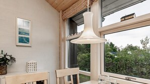 Ein Essbereich mit Holztisch, Stühlen, einer hängenden Pendelleuchte, einem kleinen weißen Schrank und einem Fenster mit Blick auf Grünflächen und ein Haus.