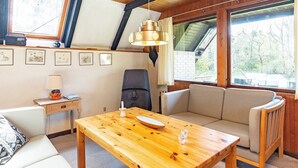 A cozy room with a wooden table, a sofa, a chair, and a desk with a lamp. There are framed pictures on the wall and a window with a view of trees. - 6 Person Holiday Home in Hals-by Traum (Hals)