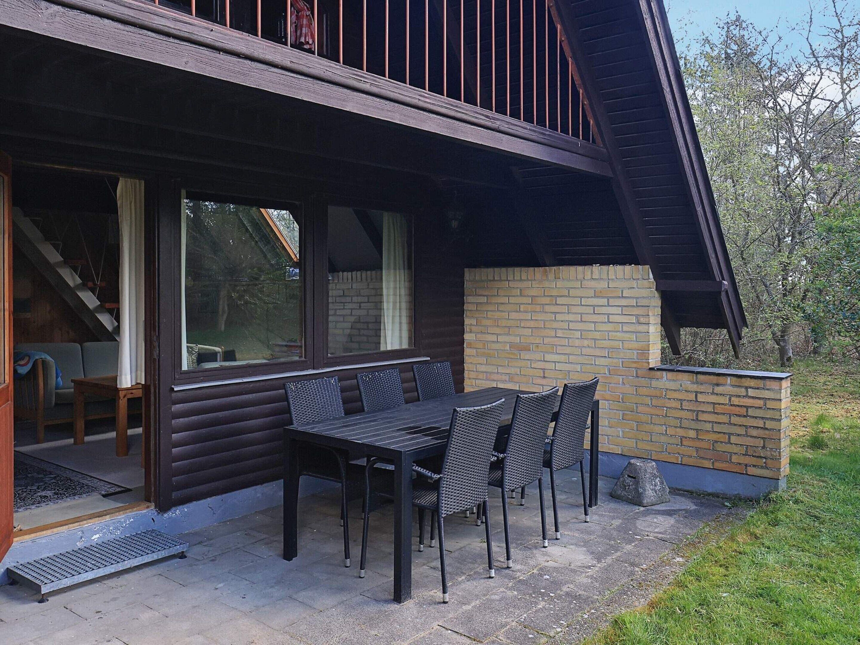 An outdoor patio with a table and chairs, a brick wall, and a wooden deck.