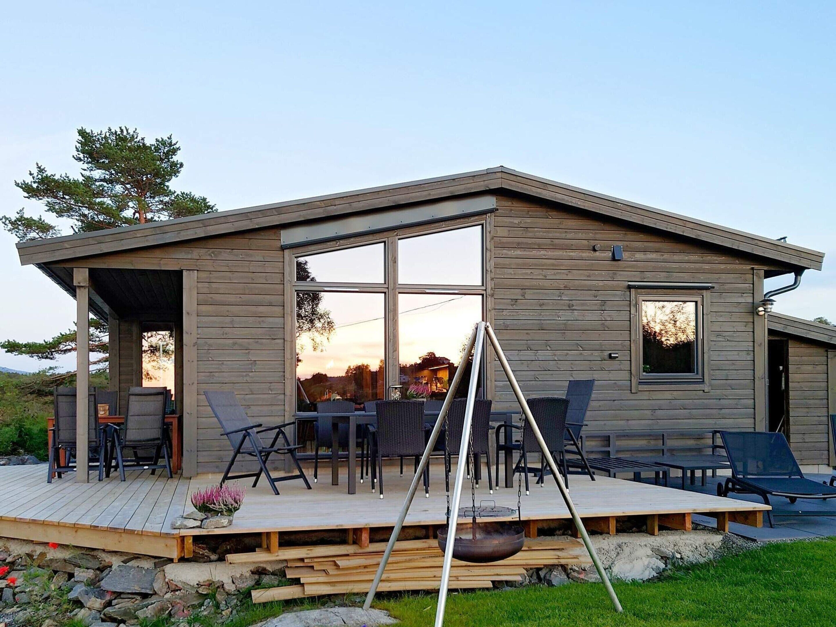 Een moderne houten hut met terras, buitenmeubels en een groot raam.