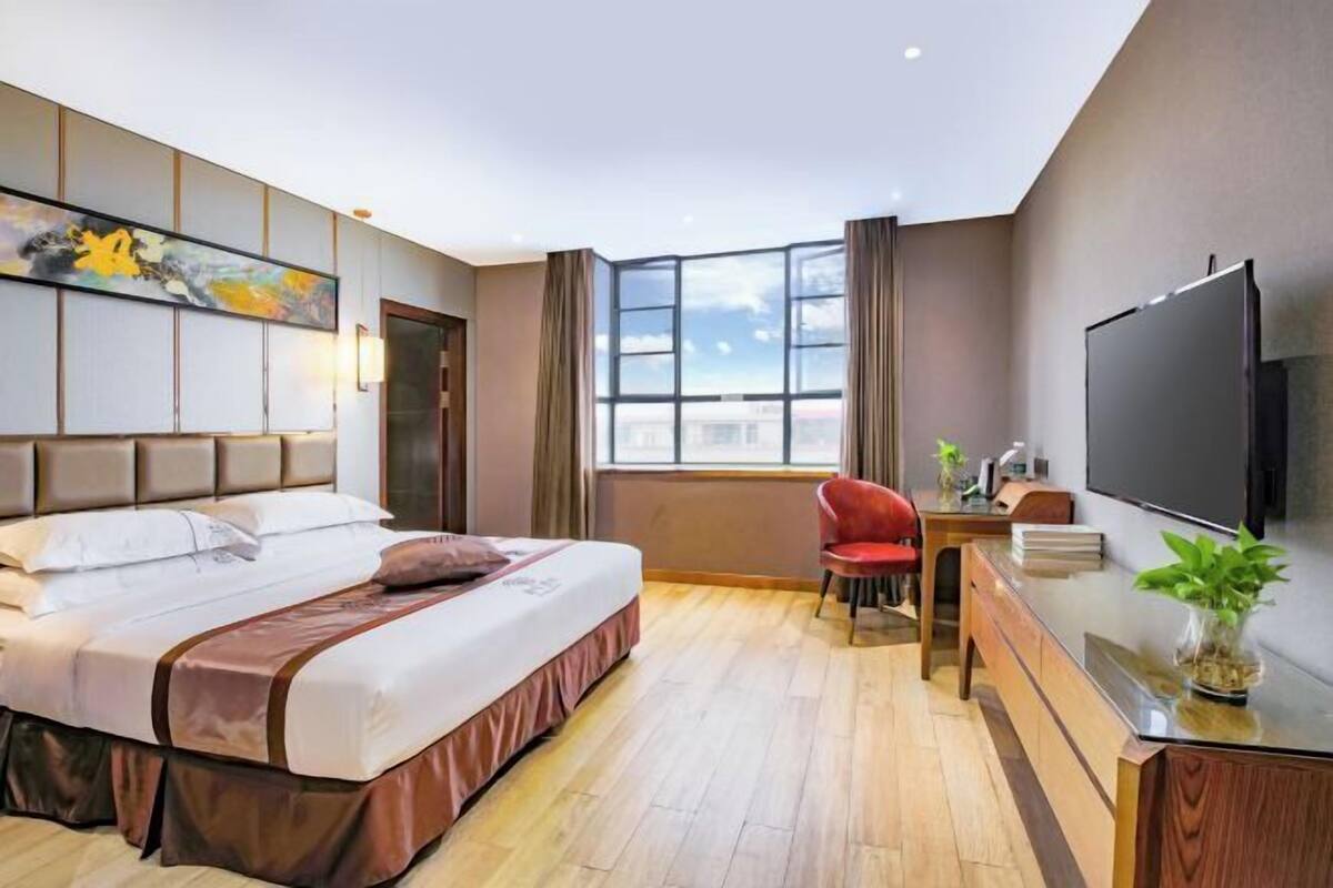 A hotel room with a bed, a desk with a chair, a TV, and a window with curtains.