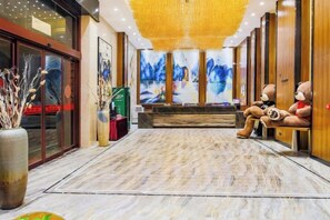 A hotel lobby with a reception desk, plush seating, and a large vase with decorative branches. - Huangting Hotel (Xintian)