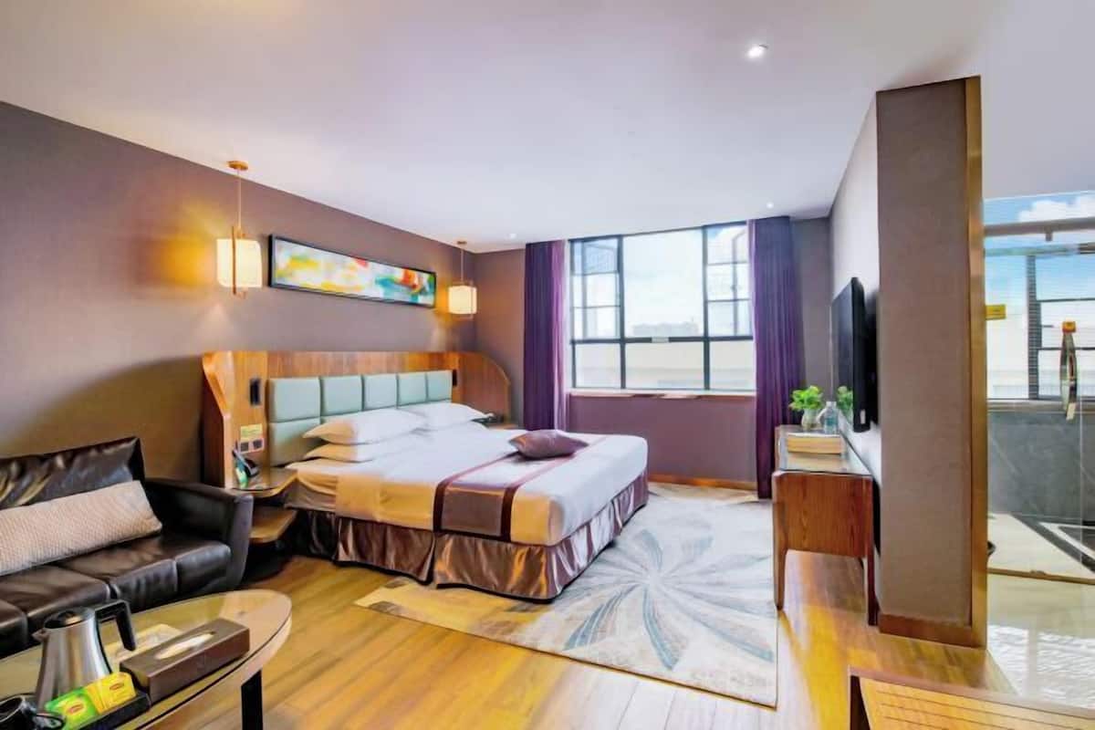 A hotel room with a bed, a sofa, a coffee table, a TV, and a window with curtains.