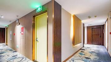 A hotel hallway with a patterned carpet, a door with an emergency exit sign, and a wall-mounted light fixture.