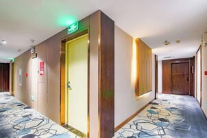 Un pasillo de hotel con alfombra estampada, una puerta con letrero de salida de emergencia y un aplique en la pared.