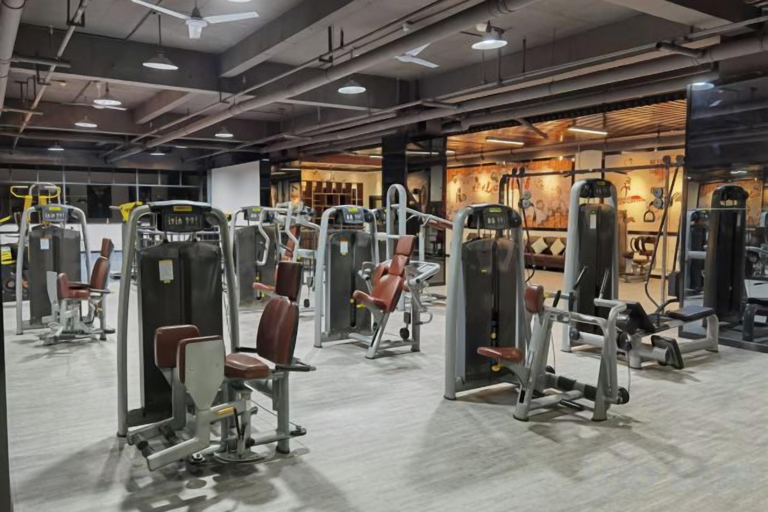 Un gimnasio con diversas máquinas de ejercicio, un espejo grande en la pared y una iluminación brillante.