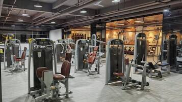 Un gimnasio con diversas máquinas de ejercicio, un espejo grande en la pared y una iluminación brillante.