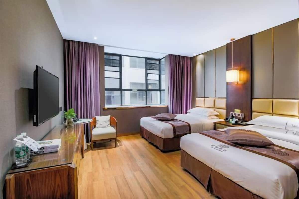 A hotel room with two beds, a desk with a TV, a chair, and a window with curtains.