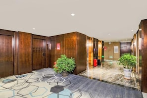 A hotel lobby with wooden paneling, a patterned carpet, and potted plants. - Huangting Hotel (Xintian)