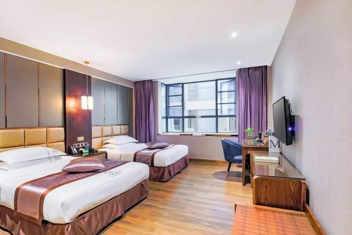 A hotel room with two beds, a desk, a chair, a TV, and a window with curtains.
