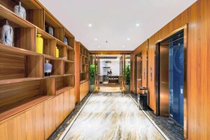 En hotellkorridor med träpanel på väggarna, marmorgolv och en receptionsdisk längre bort.