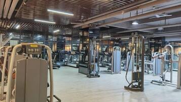 A gym with various exercise machines, a mirrored wall, and a wooden floor.